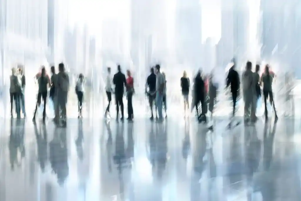 Silhouettes floues de passants en mouvement dans un hall lumineux, effet de filé traduisant l’anonymat urbain. Illustration du poème « Exister » d’Hervé Gransart.