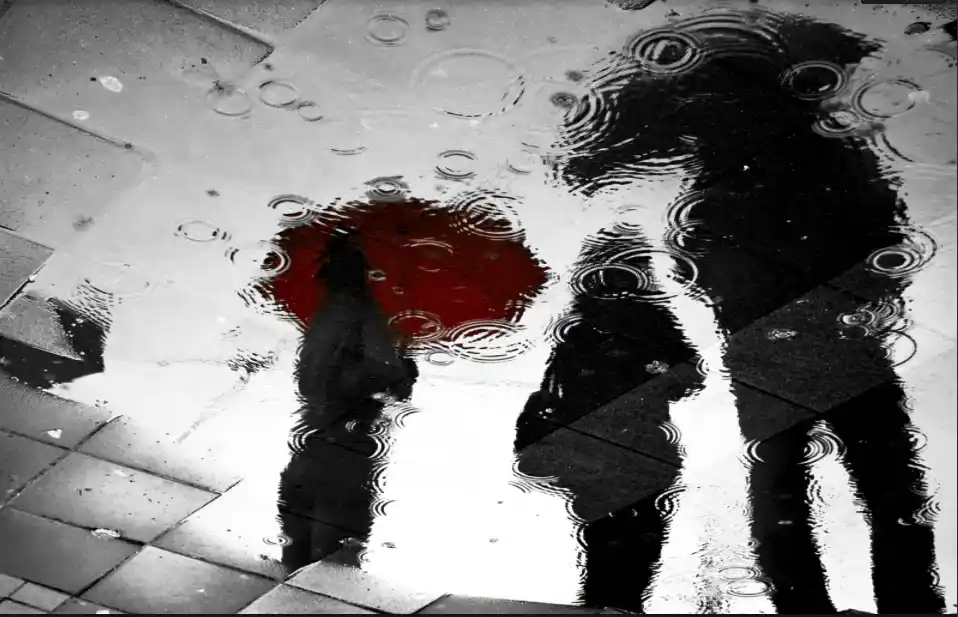 Reflet d’un parapluie rouge et de silhouettes sur un trottoir mouillé par la pluie. Illustration du billet d’humeur Ploc d’Hervé Gransart.