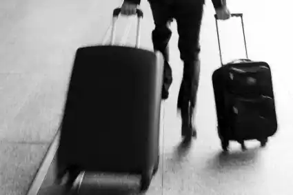Voyageur tirant deux valises à roulettes dans un hall de gare, flou de mouvement. Illustration de la chronique satirique Les Valises d’Hervé Gransart.