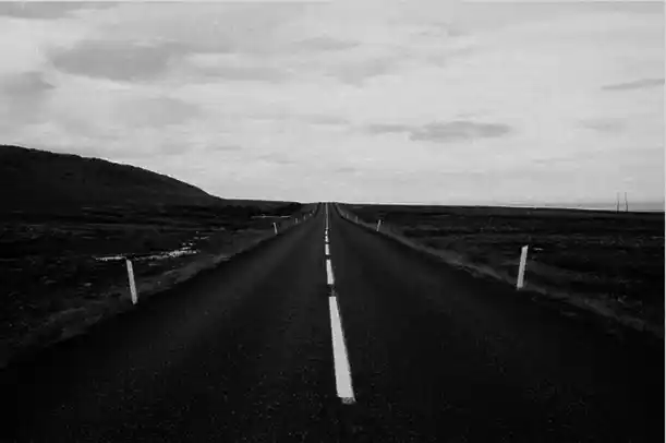 Route droite et déserte filant vers l’horizon sous un ciel nuageux, en noir et blanc. Illustration du poème « Une Autre Vie » d’Hervé Gransart.