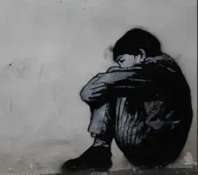 Graffiti en noir et blanc d’un enfant recroquevillé contre un mur, tête enfouie dans les genoux. Illustration du texte « Contre le mur » d’Hervé Gransart.